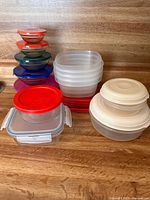 Glass and plastic food storage containers with lids of various sizes and colors stacked on wooden surface