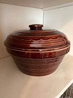 Full view of the brown glazed Marcrest stoneware Dutch oven with lid showing embossed patterns and knob handle.