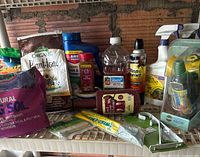 Image shows several bags of potting soil, including Star Harbor Blend and Espoma Organic Plant-tone, along with multiple bottles and spray containers of gardening chemicals and supplies on a shelf.