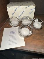 Four clear glass floating tealight candle holders, each with a white tealight candle, with original Princess House box and instruction leaflet on display.