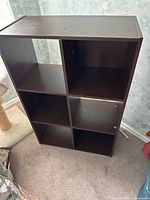 Front and side view of the brown wood storage shelf with 6 cube cubbies placed on carpet against a blue textured wall.