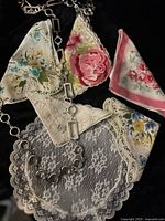 Top view of five vintage handkerchiefs with varied floral prints and lace detailing, alongside a silver-tone chain belt with circular and rectangular links