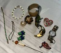 Full lot displaying various pieces of vintage costume jewelry including brooches, necklaces, a watch, and a heart-shaped box.