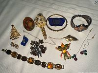 Photo of assorted vintage costume jewelry pieces including brooches, bracelets, a watch, and necklaces arranged on a white cloth.