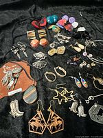 Full lot of vintage jewelry items displayed on black cloth including various earrings and cowboy themed accessories
