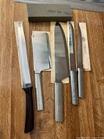 Photo of vintage RADA and Quikut cutlery set showing knives with metal handles and sheaths alongside sharpening stone and serrated knife with black plastic handle