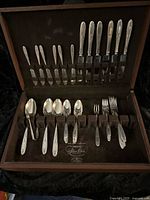 Full view of flatware set open in original box, showing knives, forks, spoons, and additional utensils organized in velvet-lined slots.