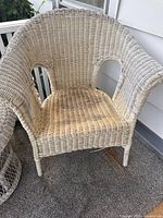 Light-colored wicker chair seen without cushion on carpeted porch floor.