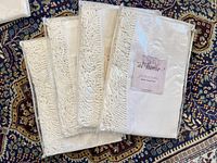 Five ivory curtain panels with bullion fringe trim folded and packaged in clear plastic bags, labeled as Soft Surroundings 'At Home' collection.