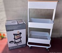 Unopened black Lexington 3-tier rolling cart with box and assembled white rolling cart side by side
