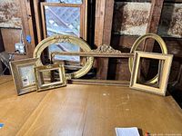 Seven gold finish vintage style frames of varied sizes and shapes arranged on a wooden surface, including rectangular and oval styles with ornamental details.