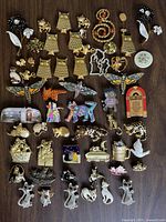 Top-down photo of 50+ assorted vintage brooches including multiple owl-shaped gold-tone brooches, colorful enamel dogs, butterflies, floral, and cat-themed pieces in gold-tone and rhinestone styles.