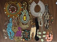 Full lot view showing variety of bold tribal and boho necklaces including chunky multicolor bead collar, seed bead layered pieces, and stone pendant necklaces on wooden background.