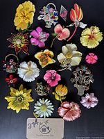 Full overview of 24 vintage floral brooches arranged on black background showing variety of colorful enamel and rhinestone designs