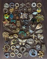 Overhead photo of 50+ vintage brooches and pins on a wooden surface showing assortment and condition.