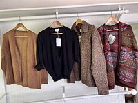Four women's XL sweaters hanging on a rack, showing different colors and styles including a brown cardigan, black cardigan, marled button-up, and patterned knit cardigan