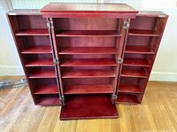 Fully opened cherry wood cabinet showing four columns of shelving inside with two door panels open flat, revealing ample shelf space.