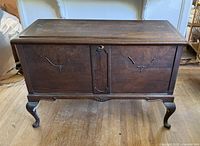 Front view of wooden chest showing carved front panels and Queen Anne legs