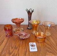 All seven carnival glass pieces arranged on wood surface, showing colors, shapes, and sizes