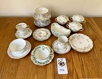 Full lot overview showing the various teacups, saucers, plates, and covered bowls on wooden table.