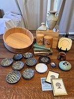 Photo showing entire lot including large wooden bowl, ceramic dishes, tea canisters, vase, lamp base, incense holder, trinket box, jade finial, bone china plate, decorative dish, books, and bookplates.