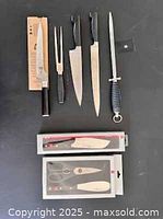 Top-down view: Shun offset bread knife in packaging; Zwilling carving fork; Zwilling 8" chef’s knife; Zwilling 10" carving/slicing knife; honing steel; two sealed boxes (kitchen shears & spreader)