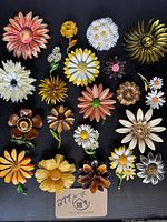 Top view of the full lot of 21 colorful vintage enamel flower brooches on black background.