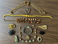 Photo showing the full assortment of 13 vintage costume jewelry pieces spread on a wooden table including multiple necklaces and brooches.