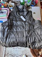 Black lightweight quilted puffer jacket laid on table with tags attached