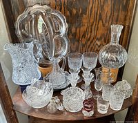 Photo of entire glassware collection showing various clear cut glass items including pitchers, decanter, glasses, bowls, and a red votive holder.