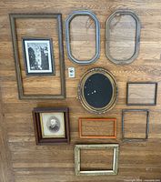 All ten picture frames laid out on wood floor showing variety in size, shape, style, and finish with some frames containing vintage photos and glass