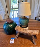 Photo showing all three items: green-glazed ginger jar with wood lid, matching jar converted to lamp with white fabric shade, and carved wooden headrest.