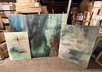 Lot of three large abstract expressionist paintings in a storage setting, showing varying sizes and moody tones.