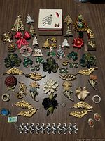Top-down photo showing the entire lot laid out in rows, including holiday-themed pins, floral pins, gold leaves, and boxed Anne Klein set