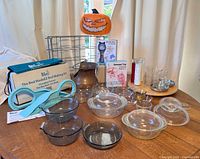 Overview image showing full lot on wooden table including glassware, metal wine rack, copper ash scuttle, bed-making kit, candle holders, Halloween topper, and toys.
