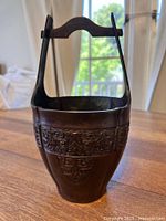 Angled front view showing full basket form, handle raised, and taotie relief detail band around the midsection.