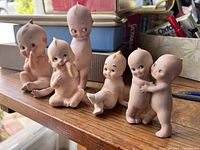 Photo of six vintage Kewpie dolls in various poses and expressions on a wooden surface.