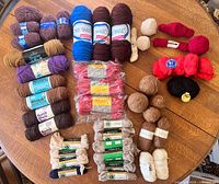 Photo showing assorted yarn skeins and balls in various colors and fibers arranged on a wooden table