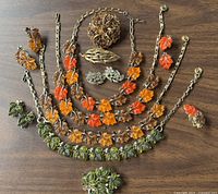 Overview of entire jewelry lot laid out on wood surface showing necklaces, brooches, and earrings with autumn leaf motifs.