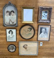 Overview of all 8 framed portraits on wooden floor in natural light showing variety of frames, photos including children and women, vintage styles