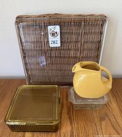 Setup of all lot items arranged together on a wooden surface: yellow Fiesta pitcher, two amber glass containers with lids, and a square glass tray propped behind them.