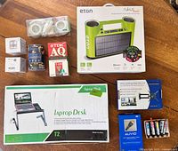 Photo of all items displayed on wooden table including boxed laptop desk, Bluetooth speaker, wall mount, HDMI cables, VHS tape, deodorizers and LED lights.