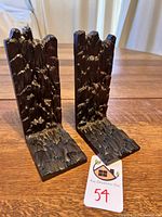 Pair of dark bronze tone cast metal bookends with textured rocky cliff face surfaces on a wooden table.