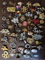 Full lot of over 50 vintage whimsical brooches laid out on wood surface showing a variety of animal, floral, and abstract designs in mixed materials.