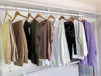 Full view of the hanging clothing lot items including pants, blouses, and sweaters with tags visible.