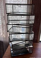 Stack of six Pottery Barn glass and mirror display boxes arranged vertically, showing clear glass, mirrored bottoms, and brass-tone frames with hinged lids.
