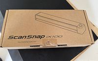 Closed original cardboard box packaging of the Fujitsu ScanSnap iX100 scanner showing product branding.
