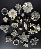Full lot of 18 vintage silver tone brooches showing variety including rhinestone, enamel, mother of pearl floral and abstract designs