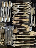 Overhead view of all flatware pieces arranged on black cloth showing spoons, forks, knives and spreaders