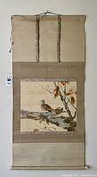 Full view of the rolled scroll showing the entire bird and branch painting with fabric borders and hanging string at the top.